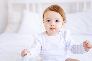 a large portrait of a cute and joyful baby girl in a crib in white clothes, a funny little child at home, the concept of children's goods