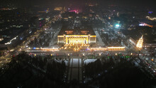 A Large Christmas Tree In The Lights On The Square. Top View From The Drone On The Street With Cars And People, A Bright Building In Garlands, Various Decorations For The New Year. Almaty, December