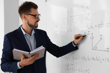 Wall Mural - Happy teacher with book explaining mathematics at whiteboard in classroom