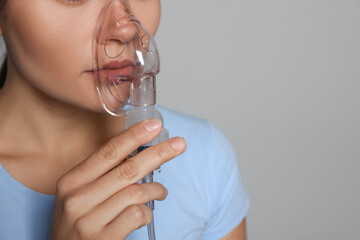 Poster - Sick young woman using nebulizer on grey background, closeup. Space for text