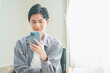 © HML - ソファに座ってスマートフォンを操作する若い男性