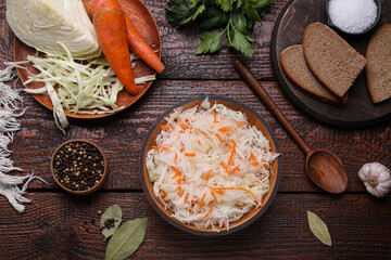 Bowl of tasty sauerkraut and ingredients on wooden table, flat lay