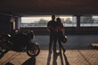© perfectlab - Young couple hugging standing by on a motorcycle in underground parking garage On the Sunset