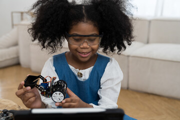 Wall Mural - Smiling child girl student learning and building project toy robotics technology at home. Girl student training and control toy robot in classroom at school