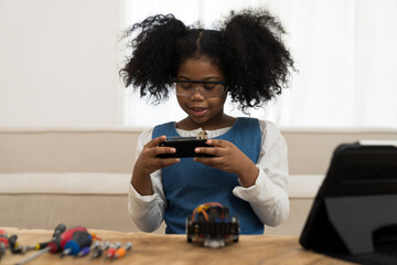 Smiling child girl student learning and building project toy robotics technology at home. Girl student training and control toy robot in classroom at school