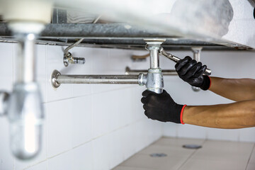 Wall Mural - Technician plumber using a wrench to repair a water pipe under the sink. Concept of maintenance, fix water plumbing leaks, replace the kitchen sink drain, cleaning clogged pipes is dirty or rusty.