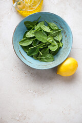 Wall Mural - Turquoise plate with fresh spinach leaves on a light-beige stone background, above view, vertical shot, copy space