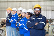 © amorn - Group of diversity male and female engineer workers at work in the industry factory and wearing safety uniform, helmet while standing with arms crossed at production line