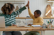 © DimaBerlin - Joyful friendly mother and biracial son giving high five sitting at kitchen table celebrating success in study. Effective good cooperation result teamwork learn motivation in homeschooling with parent
