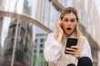Sad being victim of cyber bullying online, anxious women checks the phone, reads a message on the stairs outside from the business center. Woman shocked and clutched her head, open mouth.