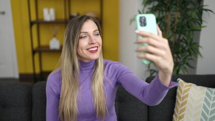 Poster - Young blonde woman having video call sitting on sofa at home