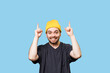 Studio portrait shot with copy space an emotional and expressive man with yellow cap pointing to free space , looking at the camera with a joyful gesture and smiling expression. blue background