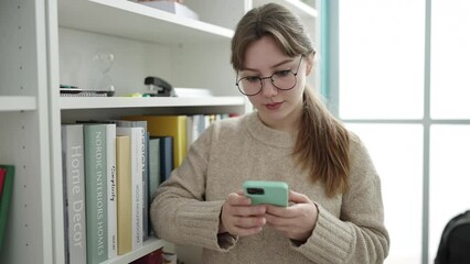 Sticker - Young blonde woman student using smartphone at library university