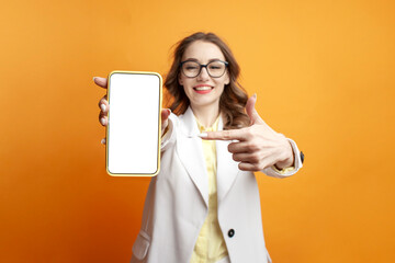 business girl in glasses and suit shows blank smartphone screen on colored background, woman manager advertises phone