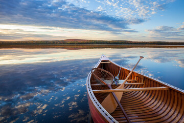 Wall Mural - wood canoe with vintage fishing rod and net on calm lake with hills with trees in autumn color in no