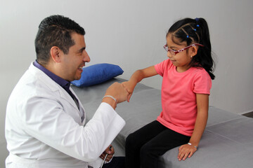 Pediatrician doctor and 4 year old latin girl patient in consultation are friends and make hi five sign and bump fists
