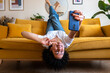 © Daniel - Joyful African American woman lying upside down on the sofa takes selfie with smart phone. Social media.