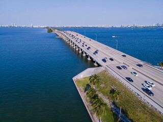 Wall Mural - Highway 195 and Florida State Road 112 against Intracoastal Waterway in Miami. Aerial view of cars traveling on a road over the inland water channel against city skyline and sky.