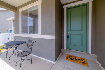 Wall Mural - Facade of a home with mint green front door and reflective sliding glass window. A steel table and chair can be seen at the porch against the gray exterior wall.