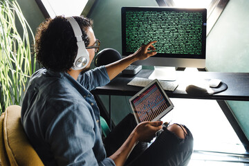 Young hispanic man programmer writing program code on desktop computer sitting at the workplace as a home office in Mexico Latin America