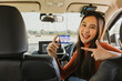 Portrait young asian woman sitting in her car show ownership of personal car license card passed test and pass exam pointing to new card with pride happy cheerful ready to drive carefree journey.