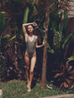 © SHOTPRIME STUDIO - A sexy woman stands on a lawn in an open swimsuit near a palm tree against the backdrop of tropical plants and palm trees, beautiful sun tanned skin, vintage style, sunny day