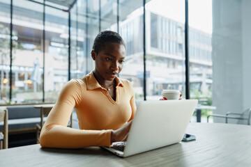 Wall Mural - Young african woman freelancer working on laptop while sitting in coworking