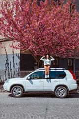 Canvas Print - woman sitting on the car blooming sakura tree on background