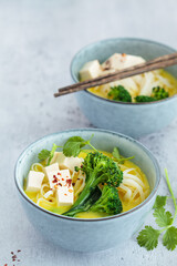 Wall Mural - Vegan laksa with rice noodles, broccoli and tofu in blue bowls, gray background.