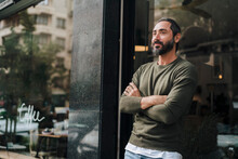 Thoughtful Man Standing With Arms Crossed In Front Of Glass Wall