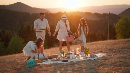 Wall Mural - Happy young parents with daughters walking for picnic in nature in summer during sunset.