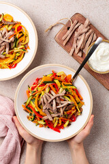 Poster - Hands holding beef tongue meat salad with marinated vegetables, bell pepper, zucchini, celery, onion, carrot. Mayonnaise sauce. Beige background. Vertical image.