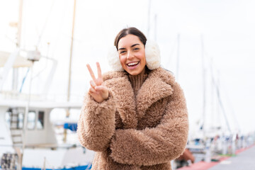 Poster - Young woman wearing winter muffs at outdoors smiling and showing victory sign