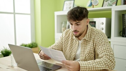 Wall Mural - Young arab man using laptop reading document looking upset at home