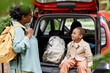 © Seventyfour - Portrait of cute black girl sitting in car trunk and enjoying travelling with mother