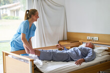 Nurse Lifting Legs Of Elderly Man Lying In Bed
