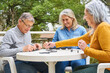 © Robert Kneschke - Senior friends playing dominoes at table in garden of nursing home