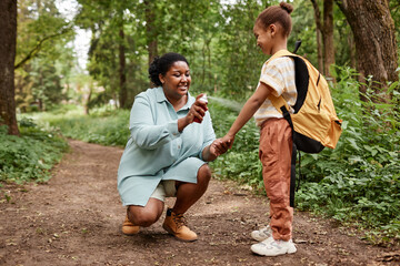 Side view portrait of black mother and daughter hiking together and using bug spray 