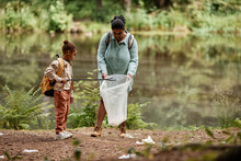 Full Length Portrait Of Eco-activist Mother And Daughter Cleaning Urban Trash By River, Copy Space 