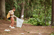 © Seventyfour - Side view portrait of eco activist little girl picking up plastic bottles in nature trail, copy space