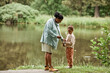 © Seventyfour - Full length portrait of black mother and daughter fishing together by river and enjoying nature outdoors, copy space