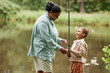 © Seventyfour - Side view portrait of happy mother and daughter fishing together by river and enjoying nature