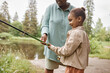 © Seventyfour - Side view portrait of happy little girl  fishing with parent by river in beautiful bonding moment