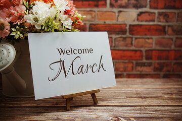 Canvas Print - Welcome March text with flower bouquet decoration on wooden and old brick wall background