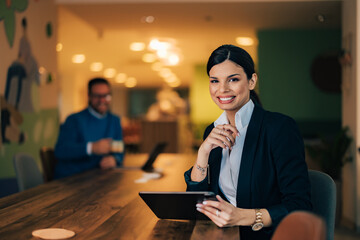 Portrait of a smiling woman and a male colleague in the background, taking a work break at the office.