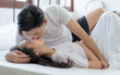 © Basicdog - Asian couple hugging and kissing each other's cheeks as they lie in bed in the morning.