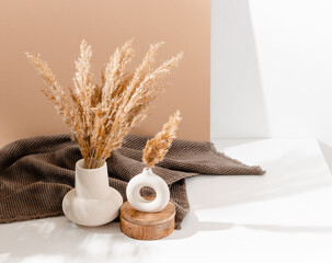 Ceramic vase set with pampas grass on the table with brown towel at the background and copy space, bohemian style, cozy shadows. Scandinavian home interior decoration