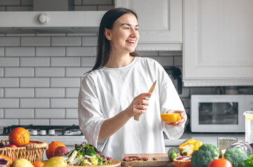 Wall Mural - Attractive young woman cutting vegetables for salad in the kitchen.