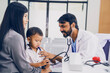 © Supavadee - Indian male doctor using stethoscope to listen baby's heartbeat, male baby sitting with asian mother at baby check-up appointment at hospital