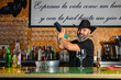 © Rafa - hombre barman con gorro de vaquero preparando un cóctel azul en la barra del bar